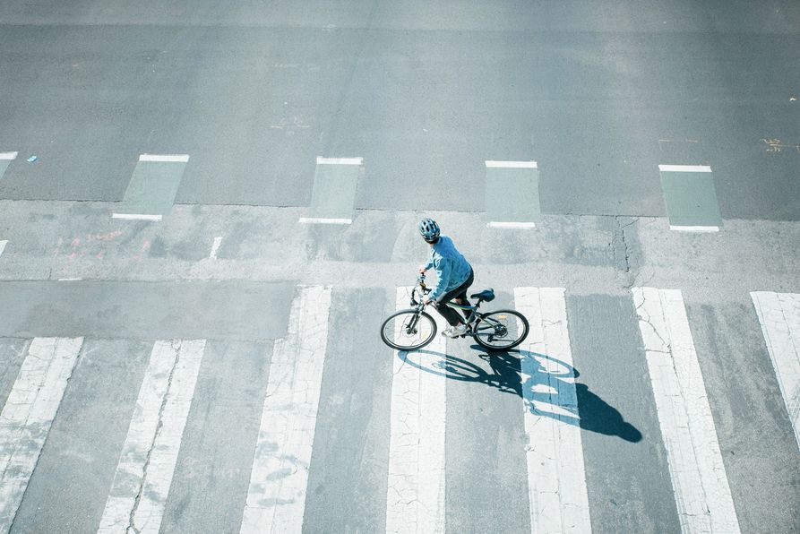 Person mit Helm auf Fahrrad überquert Zebrastreifen auf Straße aus Vogelperspektive